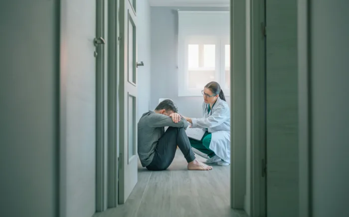 Doctor reassuring and helping to patient sitting on room floor